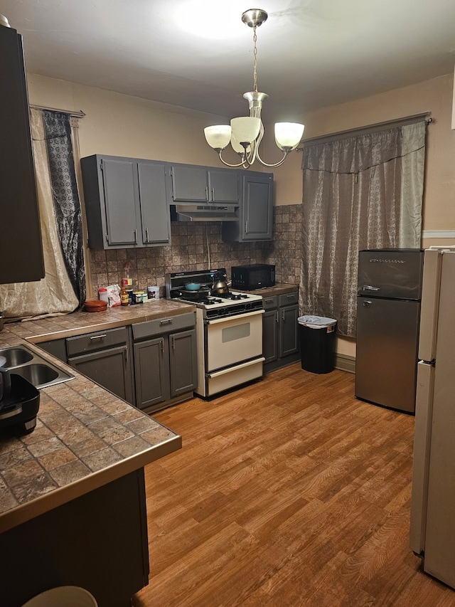 kitchen featuring white appliances, gray cabinets, backsplash, light hardwood / wood-style floors, and decorative light fixtures