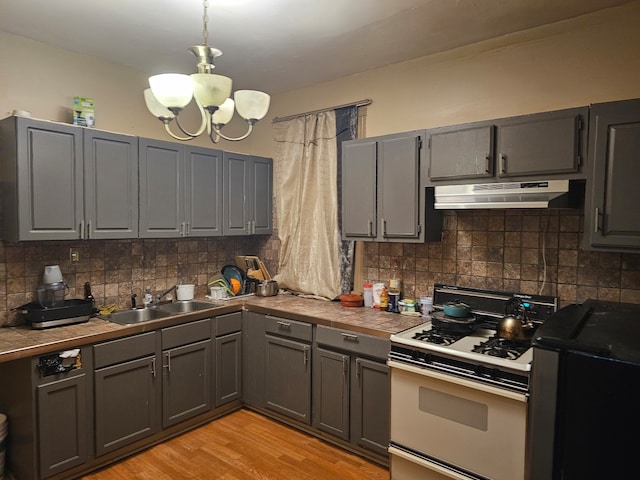 kitchen with sink, gas range gas stove, decorative light fixtures, light wood-type flooring, and tile counters