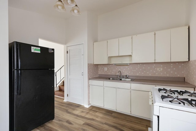 kitchen featuring sink, white gas range oven, white cabinets, black fridge, and decorative backsplash