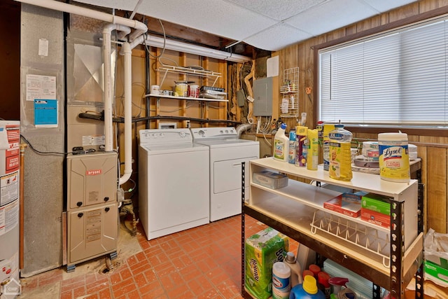 washroom with gas water heater, electric panel, washer and dryer, and wood walls