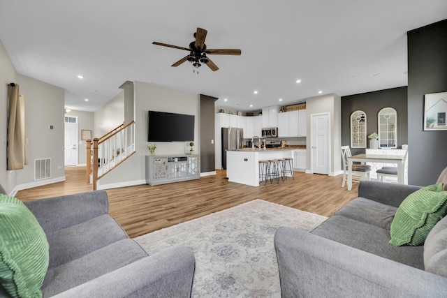 living room featuring ceiling fan, sink, and light wood-type flooring