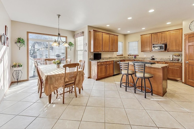 kitchen featuring sink, hanging light fixtures, stainless steel appliances, light stone counters, and a kitchen island