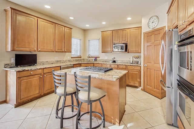 kitchen with a breakfast bar area, appliances with stainless steel finishes, a center island, light stone counters, and light tile patterned flooring