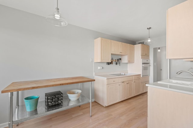 kitchen with sink, light hardwood / wood-style flooring, white oven, decorative light fixtures, and light brown cabinets