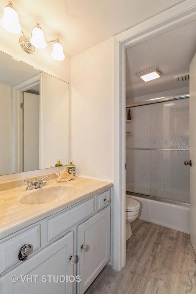 full bathroom with visible vents, toilet, combined bath / shower with glass door, vanity, and wood finished floors