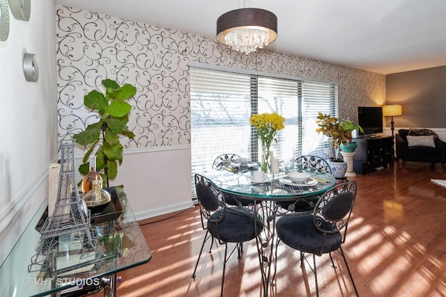 dining room featuring a chandelier, a wainscoted wall, wallpapered walls, and wood finished floors