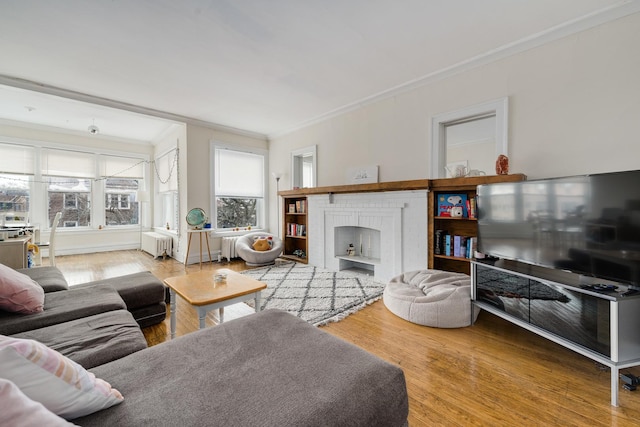 living room featuring hardwood / wood-style flooring, ornamental molding, radiator heating unit, and a brick fireplace