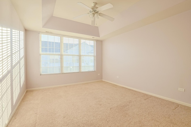 spare room featuring a raised ceiling, light carpet, and ceiling fan