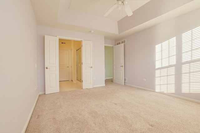 unfurnished bedroom with a raised ceiling, light colored carpet, and ceiling fan