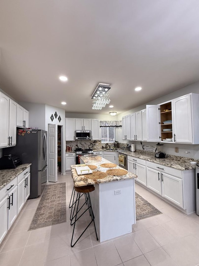 kitchen featuring light stone counters, white cabinetry, a center island, appliances with stainless steel finishes, and decorative backsplash