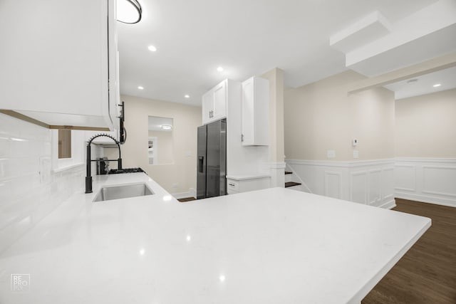 kitchen with dark hardwood / wood-style floors, stainless steel fridge with ice dispenser, white cabinetry, sink, and kitchen peninsula