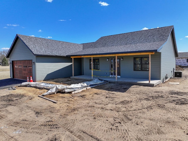 ranch-style home featuring a garage, roof with shingles, a porch, and central AC