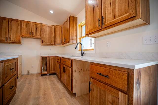 kitchen with light wood finished floors, a sink, recessed lighting, lofted ceiling, and brown cabinetry