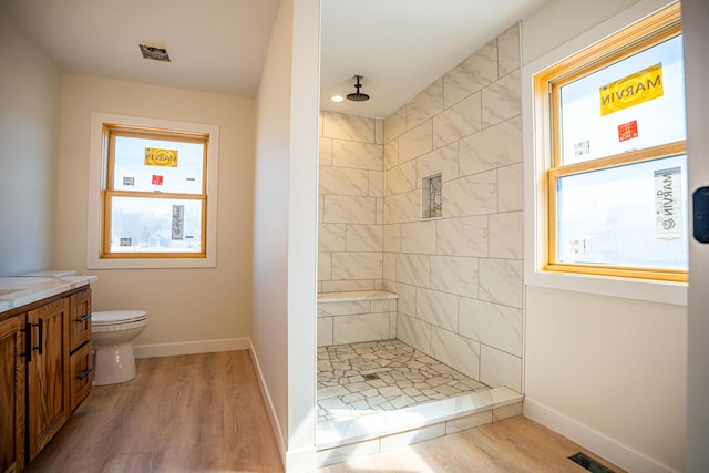 full bathroom with a tile shower, toilet, baseboards, wood finished floors, and vanity
