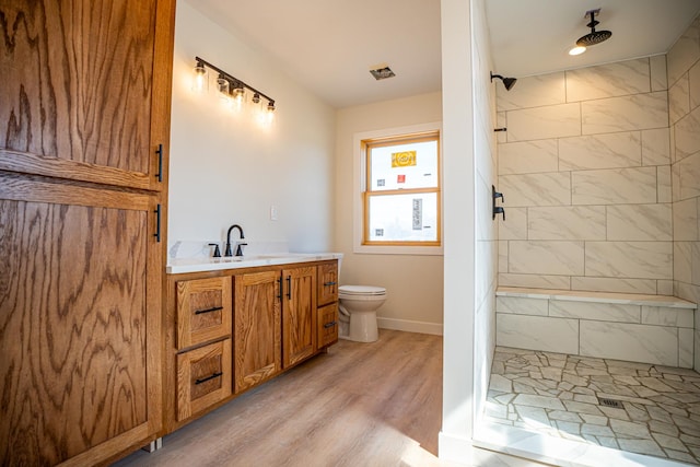 full bathroom with wood finished floors, vanity, toilet, and tiled shower