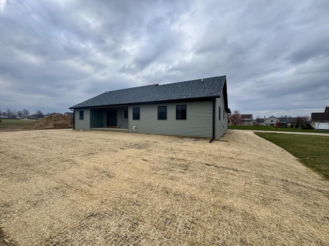rear view of property with a shingled roof and a lawn