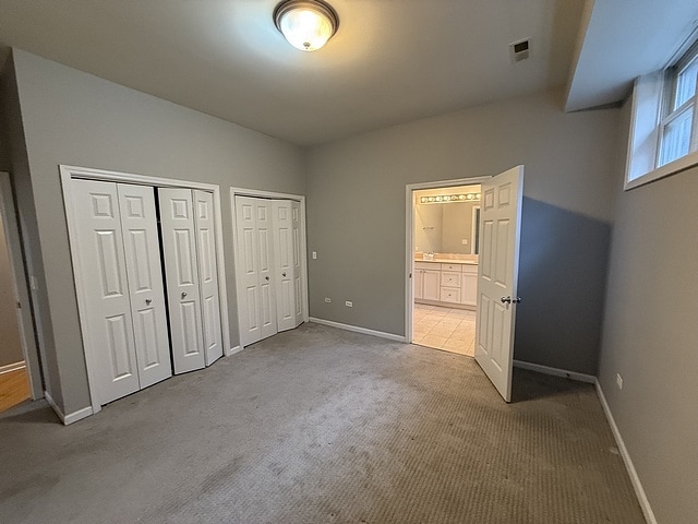 unfurnished bedroom with ensuite bathroom, multiple closets, and carpet