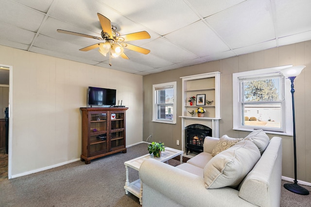 carpeted living room featuring ceiling fan, a healthy amount of sunlight, and a drop ceiling