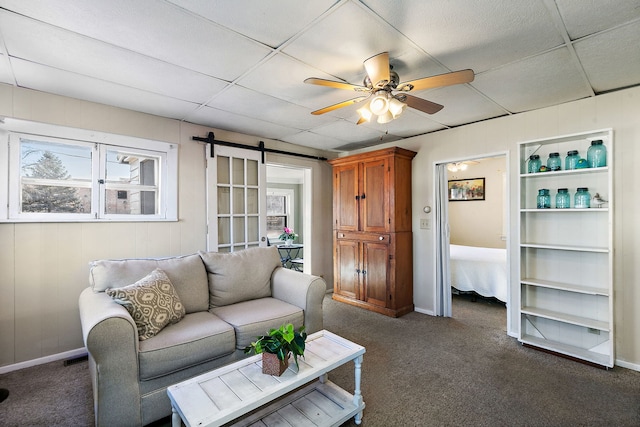 living room featuring a drop ceiling, dark carpet, a barn door, and ceiling fan