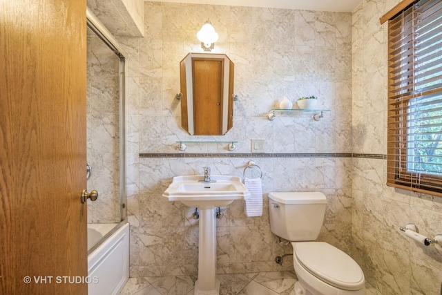 bathroom with bath / shower combo with glass door, toilet, and tile walls