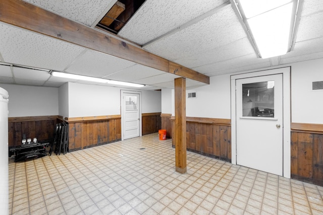 basement featuring a drop ceiling and wood walls