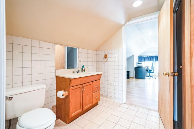 bathroom with lofted ceiling, toilet, tile walls, vanity, and tile patterned flooring