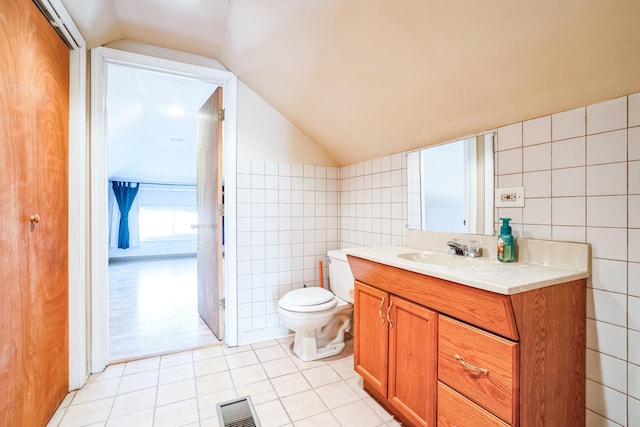 bathroom featuring toilet, vaulted ceiling, tile walls, vanity, and tile patterned flooring