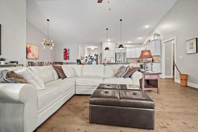 living room with ceiling fan with notable chandelier, high vaulted ceiling, sink, and light hardwood / wood-style floors