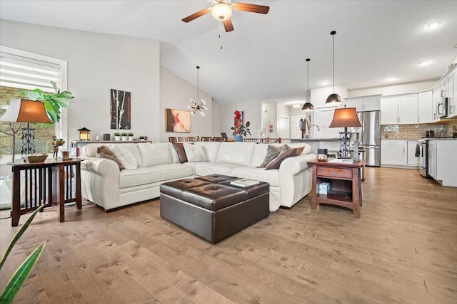 living room featuring high vaulted ceiling, ceiling fan with notable chandelier, and light hardwood / wood-style floors