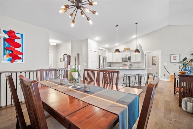 dining space with high vaulted ceiling, light hardwood / wood-style flooring, and a notable chandelier