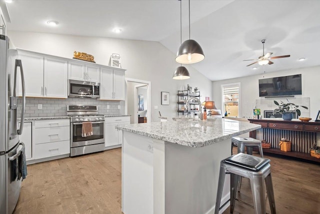 kitchen featuring white cabinetry, appliances with stainless steel finishes, decorative light fixtures, and a breakfast bar