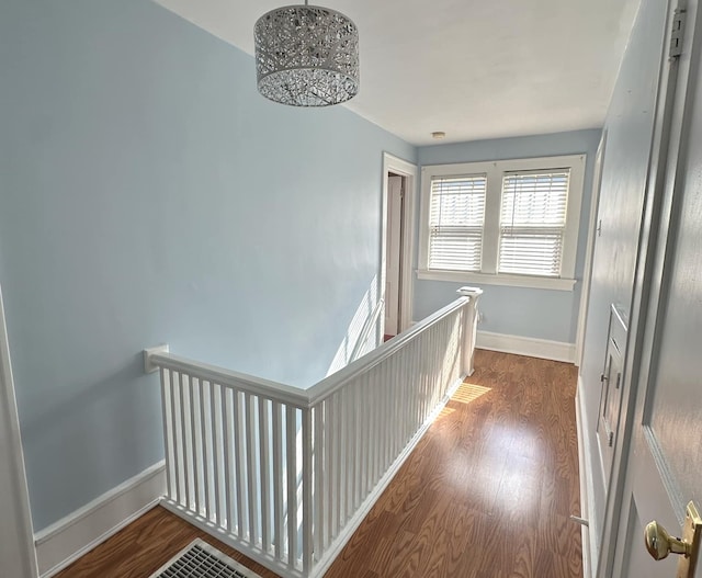 corridor with baseboards, wood finished floors, and an upstairs landing