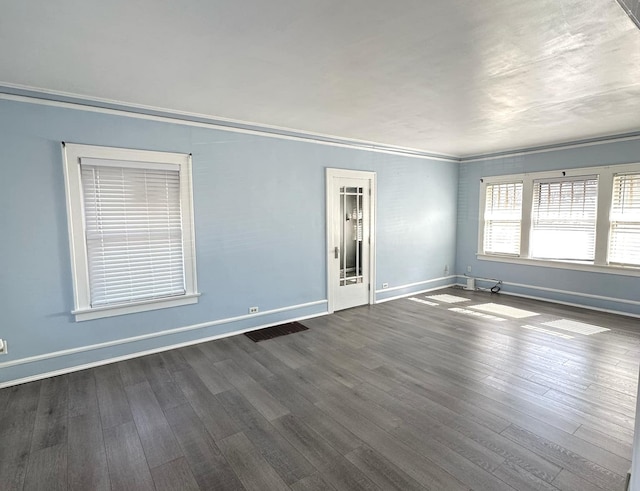 spare room with visible vents, crown molding, baseboards, and dark wood-type flooring