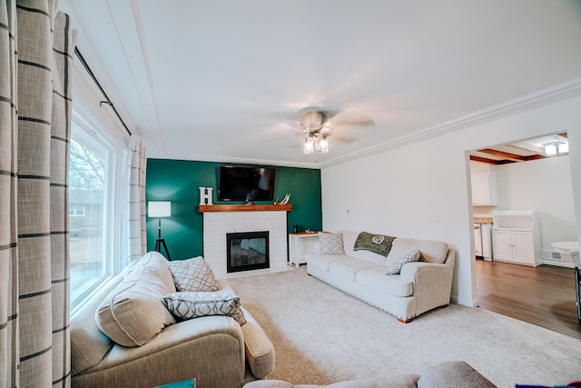 carpeted living room featuring a brick fireplace, ornamental molding, and ceiling fan