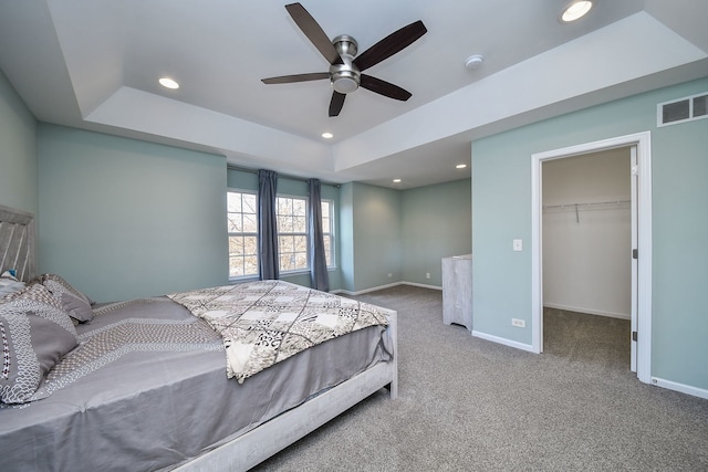 carpeted bedroom with ceiling fan, a walk in closet, a raised ceiling, and a closet