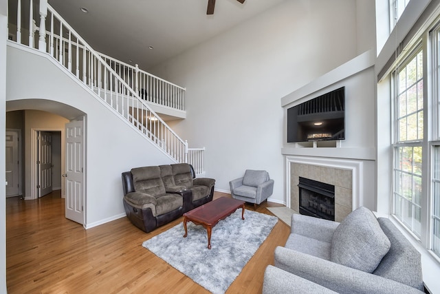 living room with hardwood / wood-style floors, a towering ceiling, a fireplace, and ceiling fan