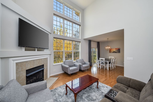 living room featuring a notable chandelier, a wealth of natural light, a tile fireplace, and light wood-type flooring