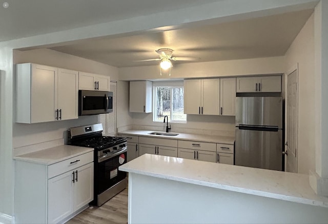 kitchen with sink, kitchen peninsula, ceiling fan, stainless steel appliances, and white cabinets