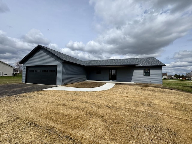 ranch-style home with an attached garage, roof with shingles, driveway, and a front lawn