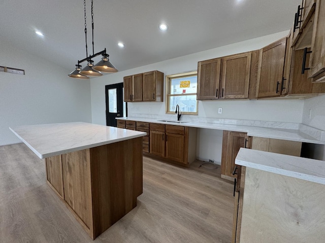 kitchen featuring light stone counters, a center island, a sink, pendant lighting, and light wood finished floors