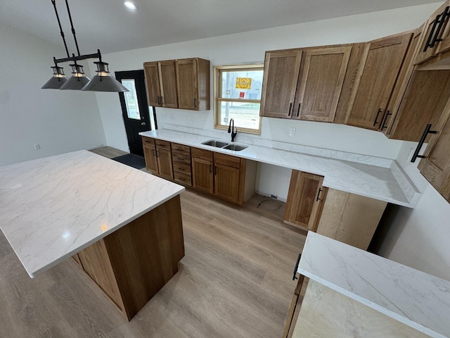 kitchen featuring a sink, light wood-style floors, decorative light fixtures, light stone countertops, and brown cabinetry