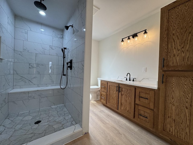 full bath featuring toilet, wood finished floors, vanity, and tiled shower