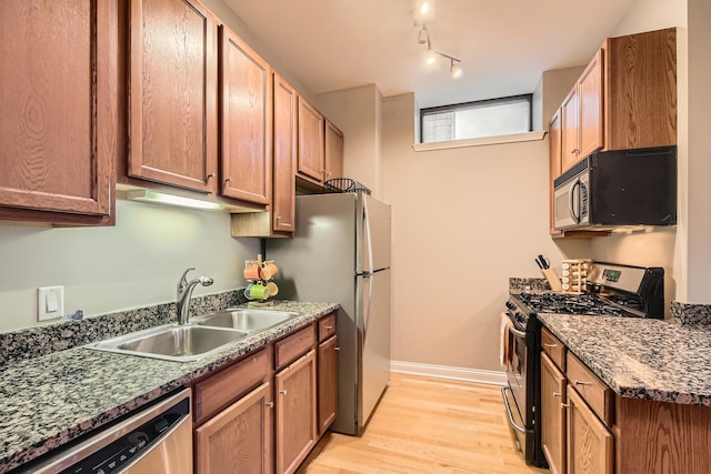 kitchen with sink, light hardwood / wood-style flooring, dark stone counters, track lighting, and stainless steel appliances