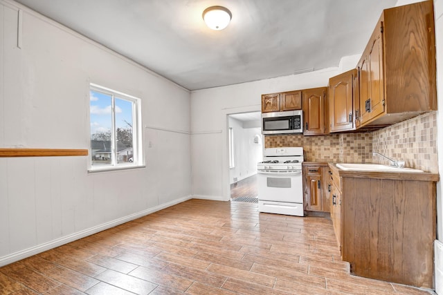 kitchen with tasteful backsplash, white gas range, light hardwood / wood-style floors, and sink