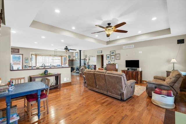 living area with a tray ceiling, light wood-style flooring, and visible vents