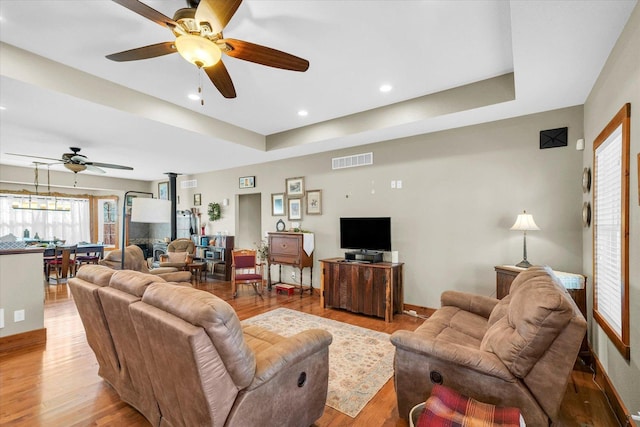 living room featuring a wood stove, light wood-style floors, visible vents, and a tray ceiling