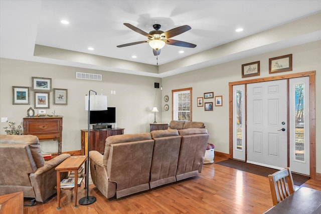 living area with visible vents, a raised ceiling, and wood finished floors