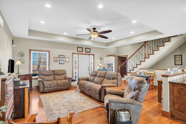 living room with light wood-type flooring, stairs, a tray ceiling, and recessed lighting