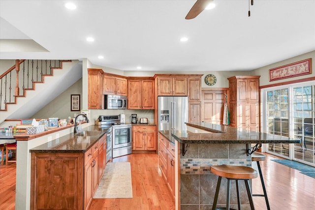 kitchen featuring a breakfast bar area, a peninsula, a sink, appliances with stainless steel finishes, and light wood finished floors