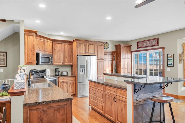 kitchen with appliances with stainless steel finishes, brown cabinets, a kitchen breakfast bar, a peninsula, and a sink